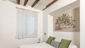 Ein Schlafzimmer mit Bett, einem Fenster mit leichtem Vorhang, einem Wandbild und einem Nachttisch.