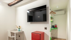 Ein Zimmer mit einem an der Wand befestigten Flachbildfernseher, einem kleinen roten Kühlschrank, einem weißen Schreibtisch mit Stuhl und einem Bett.