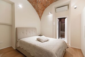 Una camera da letto con soffitto in mattoni, un letto con copripiumino bianco e un condizionatore.