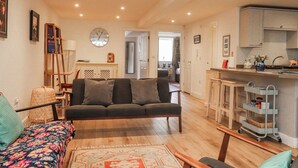 A living room with a sofa, a patterned rug, a wooden coffee table, and a kitchen area with cabinets and a cart. - Number 7 Canalside (Skipton)