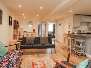 A living room with a sofa, a patterned rug, a wooden coffee table, and a kitchen area with cabinets and a cart. - Number 7 Canalside (Skipton)