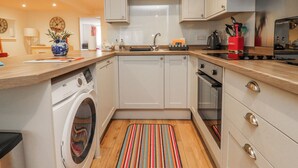 A compact kitchen with a washing machine, a sink, and a stove. - Number 7 Canalside (Skipton)