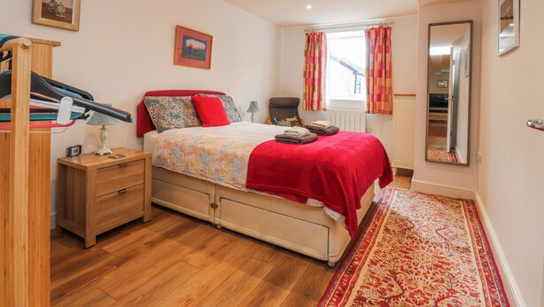 A bedroom with a bed, a wooden nightstand, a mirror, a window with curtains, and a radiator. - Number 7 Canalside (Skipton)