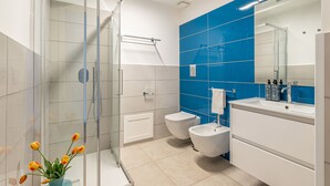 A modern bathroom with a glass shower enclosure, a white toilet, a bidet, and a sink with a mirror. - Palazzo Ferrara - Tarocco by Wonderful Italy (Palermo)