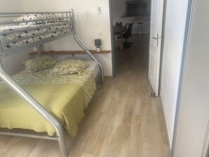 Ein Etagenbett mit Blumenoptik, ein kleiner Tisch mit Stuhl und eine Küchenzeile im Hintergrund.