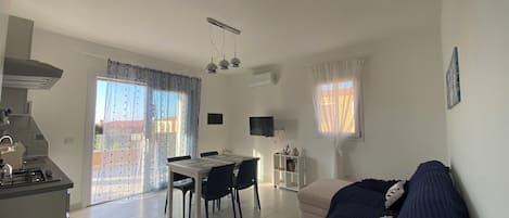 Una sala de estar moderna con un sofá, una mesa de comedor y sillas. Hay una zona de cocina con estufa y armarios.