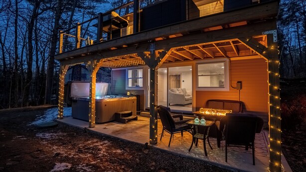 A two-story wooden cabin with a hot tub, outdoor seating, and string lights.