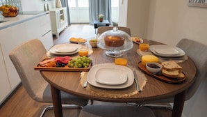 Ein Frühstückstisch mit Obstplatte, Brot und einer mit Stoff bedeckten Kuchen.