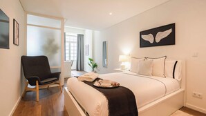 Ein Hotelzimmer mit Bett, Sessel, Nachttisch, Lampe und einem Wandbild.