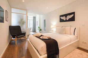 Ein Hotelzimmer mit Bett, Sessel, Nachttisch, Lampe und einem Wandbild.