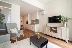Ein modernes Wohnzimmer mit einem grauen Sessel, einem schwarzen Couchtisch mit einer Vase, einem Fernseher an der Wand und einer Küche im Hintergrund.