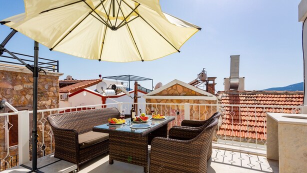 A balcony with wicker furniture, a table with fruit and drinks, and a large umbrella. - 2 bedroom Townhouse Located Heart of Kalkan Old Town (Kalkan)
