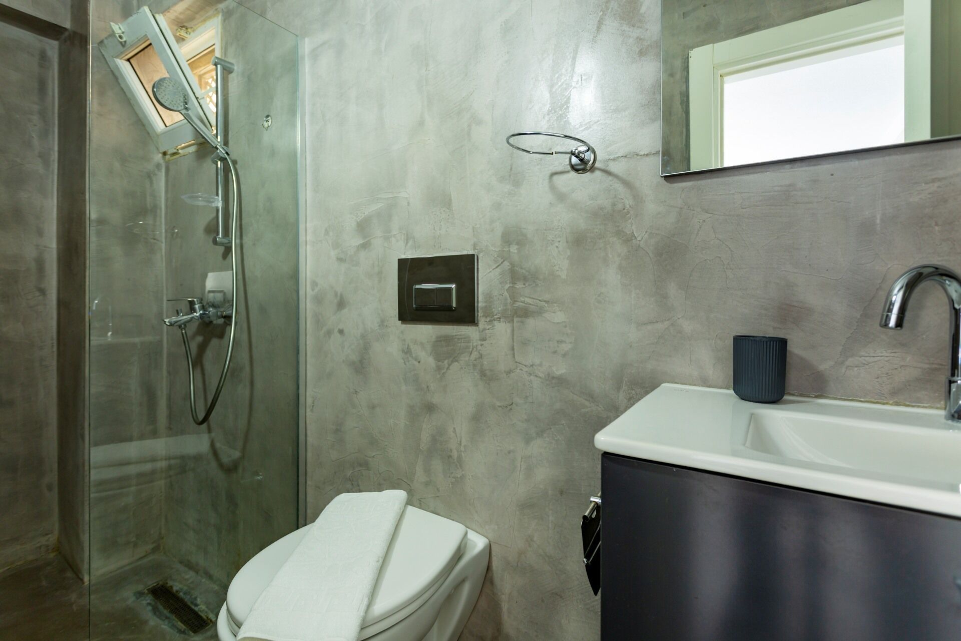 Un baño con cabina de ducha de vidrio, inodoro, lavabo con mueble oscuro y espejo sobre el lavabo.