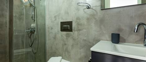 Un baño con cabina de ducha de vidrio, inodoro, lavabo con mueble oscuro y espejo sobre el lavabo.