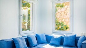 A room with a blue sofa, two windows with plants, and a stone wall. - 2 bedroom Townhouse Located Heart of Kalkan Old Town (Kalkan)