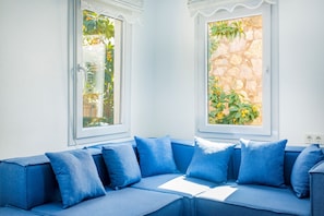 A room with a blue sofa, two windows with plants, and a stone wall. - 2 bedroom Townhouse Located Heart of Kalkan Old Town (Kalkan)