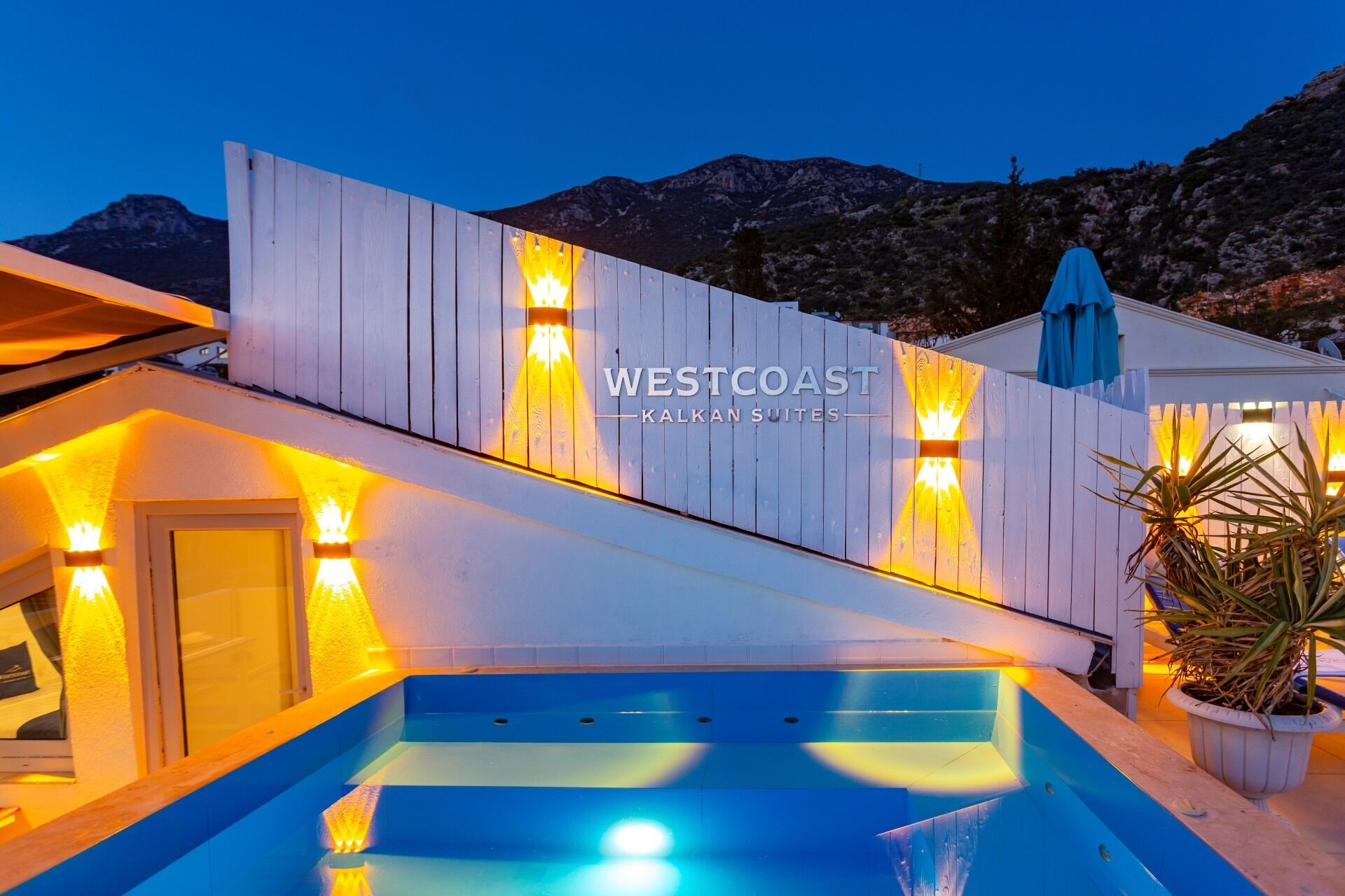 A pool area with a wooden deck and a sign reading 'WESTCOAST KALKAN SUITES'.