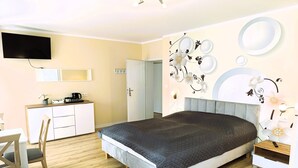 Een slaapkamer met een bed, een bureau, een stoel, een aan de muur bevestigde televisie en een deur.
