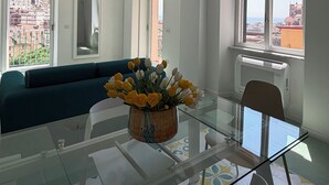 Moderni olohuone, jossa on lasinen ruokapöytä, sohva ja suuret ikkunat, joista avautuu näkymä kaupunkiin.
