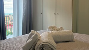 Hotellihuone, jossa on sänky, kaksi rullalle taitettua pyyhettä, ikkuna verhoilla ja näkymä rakennuksiin.