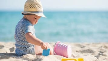Niño jugando con juguetes en una playa arenosa, con vista despejada al océano de fondo.