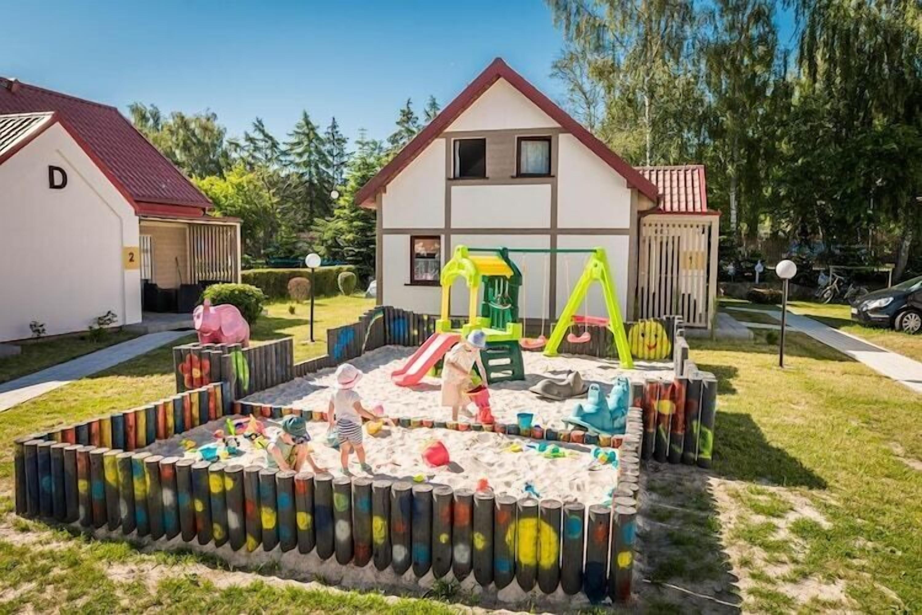 Zona residencial con una casa, un área de juegos con tobogán y columpios, y un arenero cercado.