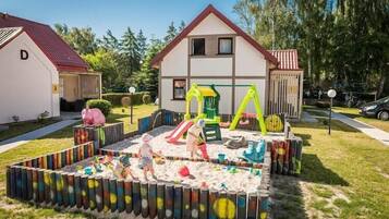 Zona residencial con una casa, un área de juegos con tobogán y columpios, y un arenero cercado.