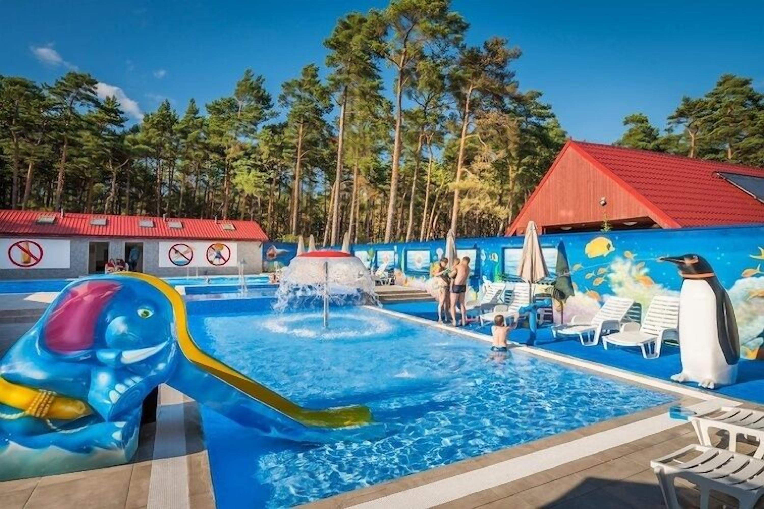 Una piscina con tobogán, sillas de descanso y un mural de pingüinos.