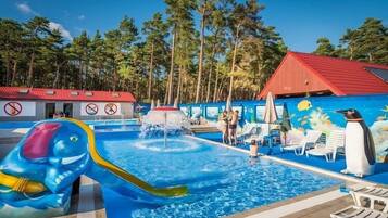 Una piscina con tobogán, sillas de descanso y un mural de pingüinos.