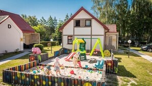 A residential area with a house, a play area with a slide and swings, and a fenced sandbox. - Comfortable holiday home, summer pool (Leba)
