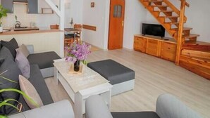 A modern living room with a sofa, a coffee table with a vase, a wooden staircase, and a TV. - Comfortable holiday home, summer pool (Leba)