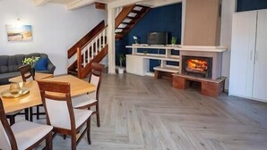 Una sala de estar con chimenea, piso de madera, una zona de comedor con sillas, un sofá y una escalera.