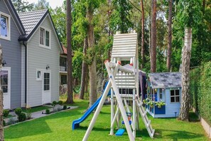 Ein Wohngebiet mit einem zweistöckigen Haus, einer Spielanlage mit Rutsche und einem kleinen, blauen Spielhäuschen.