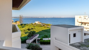 A balcony with a view of the sea, a building with a sign, and a grassy area with a pathway. - Renovated 2BR Lagos w/ Pool & Garage by Soulplaces (Lagos)