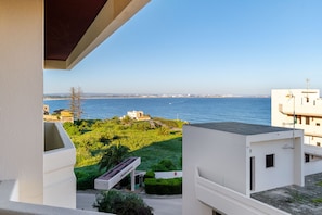 A balcony with a view of the sea, a building with a sign, and a grassy area with a pathway. - Renovated 2BR Lagos w/ Pool & Garage by Soulplaces (Lagos)
