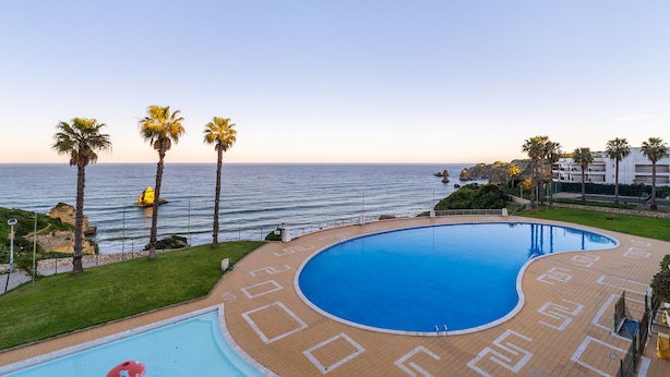 A swimming pool with a view of the sea, palm trees, and a building in the background. - Renovated 2BR Lagos w/ Pool & Garage by Soulplaces (Lagos)