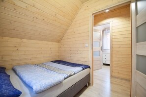 A compact wooden room with a single bed, a small bedside table, and a door leading to a bathroom.
