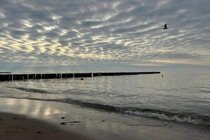 A beach with a pier extending into the water, waves gently lapping at the shore, and a bird flying in the sky. - Comfortable holiday home close to the beach (Pobierowo)
