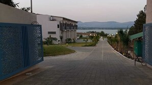 A paved pathway leading to a building with a view of a body of water and mountains.