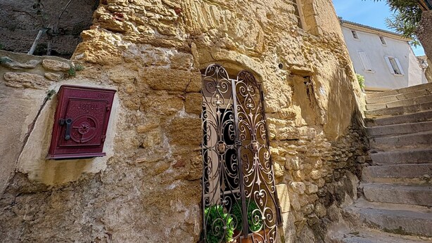 A stone building with a metal gate, a small plaque, and a staircase leading up. - L'Orée du Castel - Gîte at the foot of the castle (Châteauneuf-du-Pape)