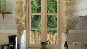 A kitchen with a double door window, a coffee maker, a sink, and a wooden cabinet. - L'Orée du Castel - Gîte at the foot of the castle (Châteauneuf-du-Pape)