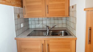 A compact kitchen with wooden cabinets, a stainless steel sink, and a tiled backsplash. - Apartment Ferienwohnungen Grossberghütte (Rio di Pusteria)