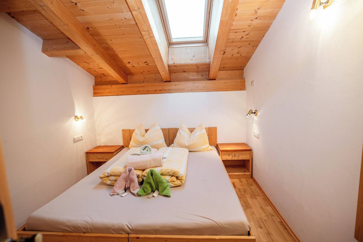 Ein Schlafzimmer mit Oberlicht, Holzbalken, einem Bett mit Kissen und Nachttischen.