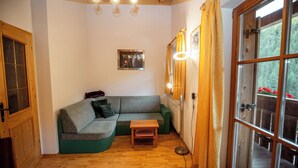 A cozy room with a wooden floor, a green sofa, a small table, and a window with curtains. - Apartment Ferienwohnungen Grossberghütte (Rio di Pusteria)