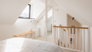 Een slaapkamer met een schuine plafond, een houten bankje, een witte ladekast en een witte balustrade.