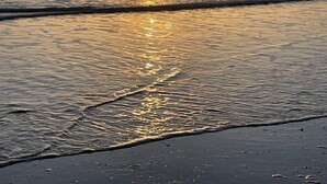 Een zonsondergang boven een strand met rustige golven en een heldere lucht.