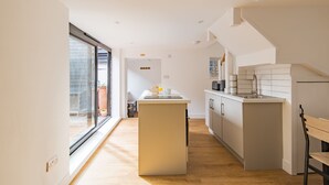 Een moderne keuken met een centraal eiland, een eethoek met tafel en stoelen, en een grote schuifdeur naar een buitenruimte.