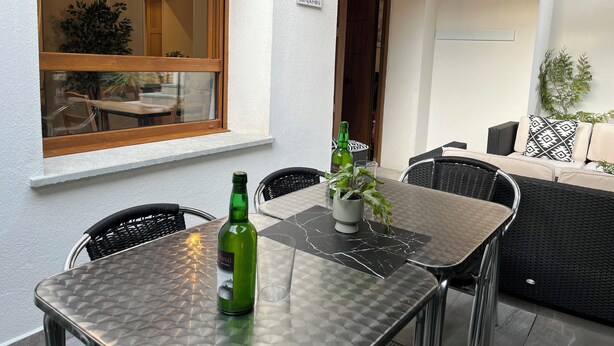 Eine Terrasse mit Tisch, Stühlen, einer Weinflasche, einem Blumentopf und einer Couch.