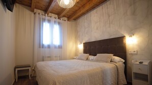 Ein Schlafzimmer mit einem großen Bett, einer Holzbalkendecke, einem Nachttisch und einer Wandleuchte.