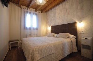Ein Schlafzimmer mit einem großen Bett, einer Holzbalkendecke, einem Nachttisch und einer Wandleuchte.